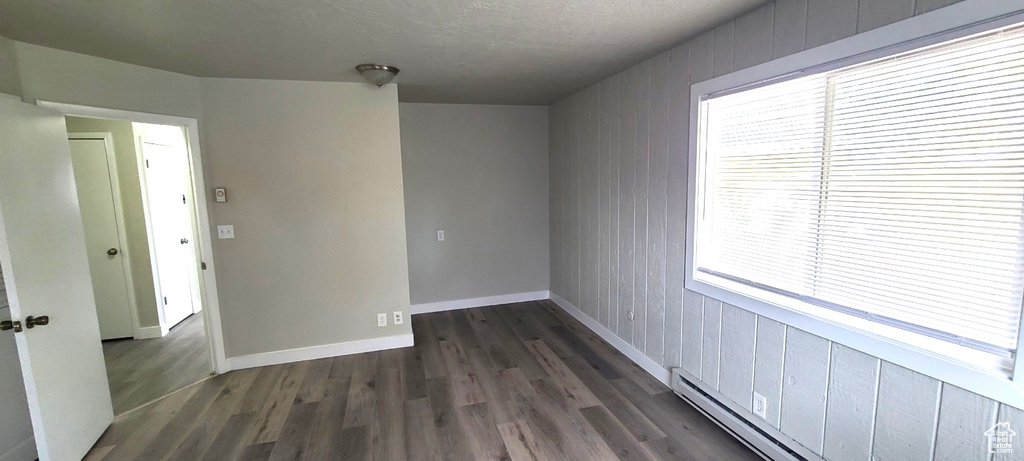 Unfurnished room with a textured ceiling, dark hardwood / wood-style floors, and a baseboard heating unit