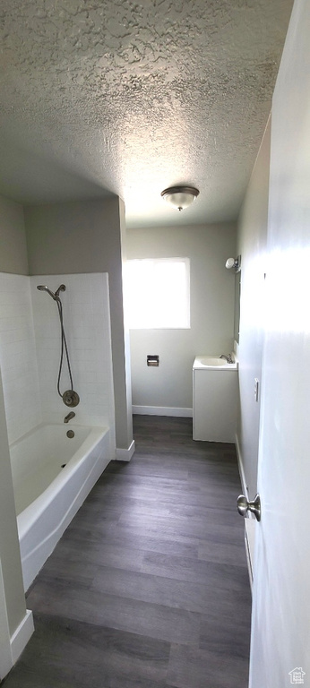 Bathroom with tiled shower / bath combo, hardwood / wood-style floors, a textured ceiling, and sink