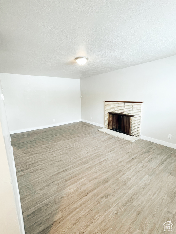 Unfurnished living room with a brick fireplace, a textured ceiling, and light hardwood / wood-style flooring
