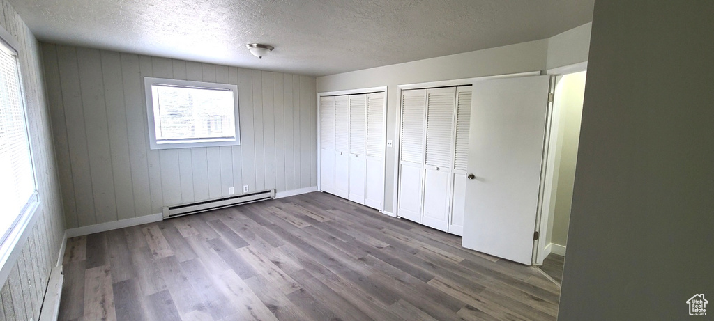 Unfurnished bedroom with dark hardwood / wood-style floors, two closets, a textured ceiling, and baseboard heating