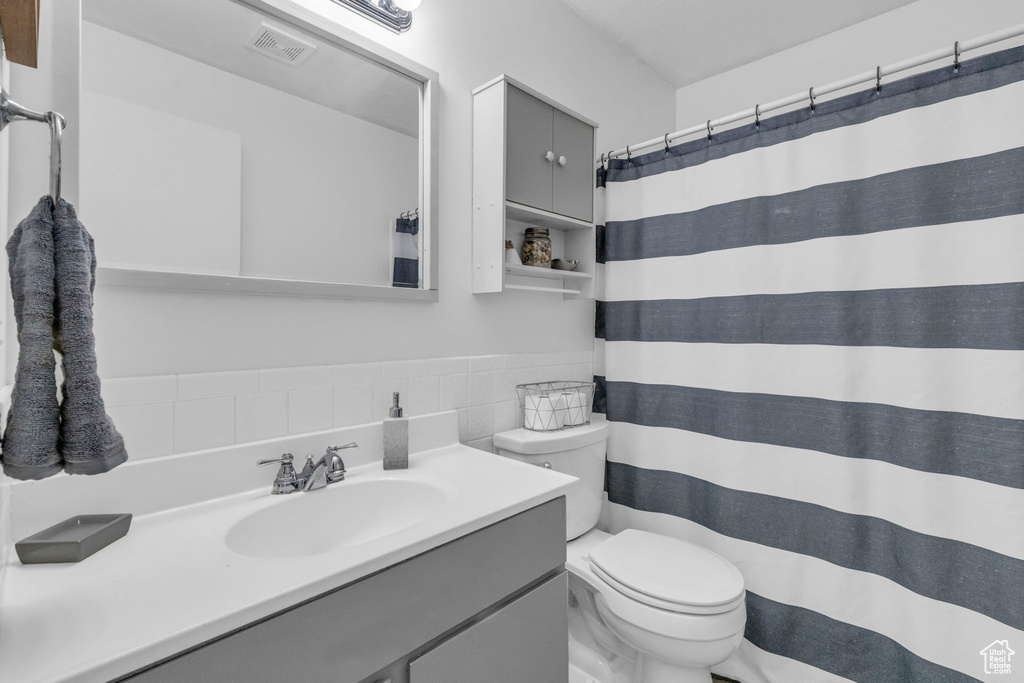 Bathroom with toilet, vanity with extensive cabinet space, tasteful backsplash, and tile walls