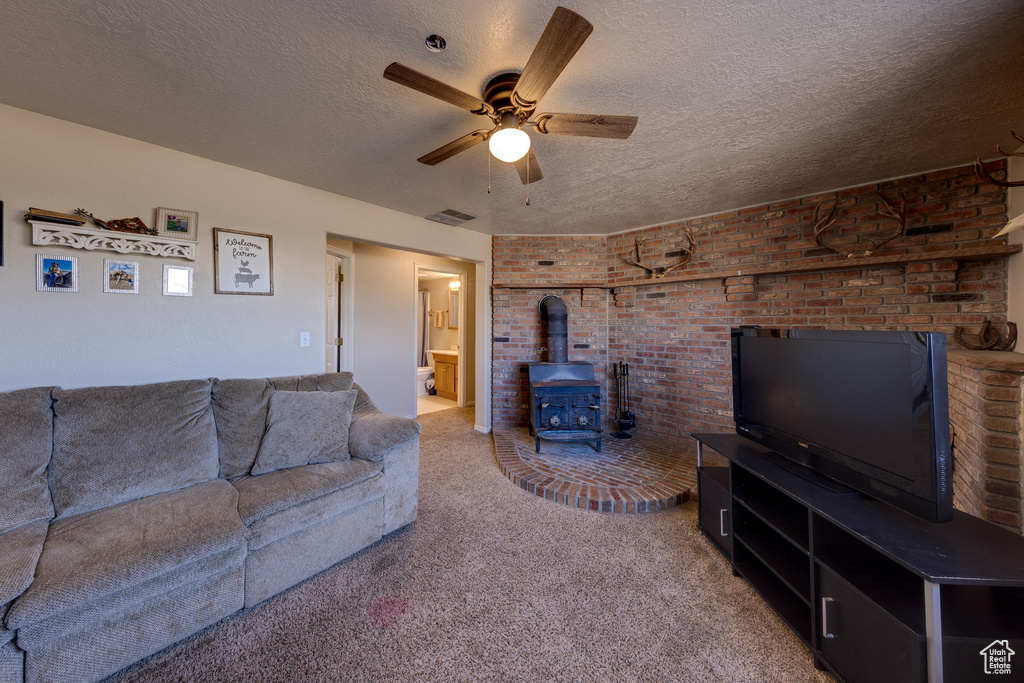 Carpeted living room featuring brick wall, a textured ceiling, ceiling fan, and a wood stove
