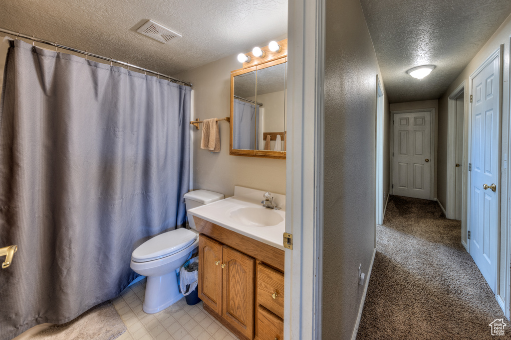 Bathroom with toilet, a textured ceiling, vanity with extensive cabinet space, and tile flooring