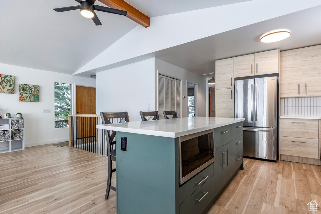 Kitchen featuring light hardwood / wood-style flooring, stainless steel appliances, vaulted ceiling with beams, and a breakfast bar