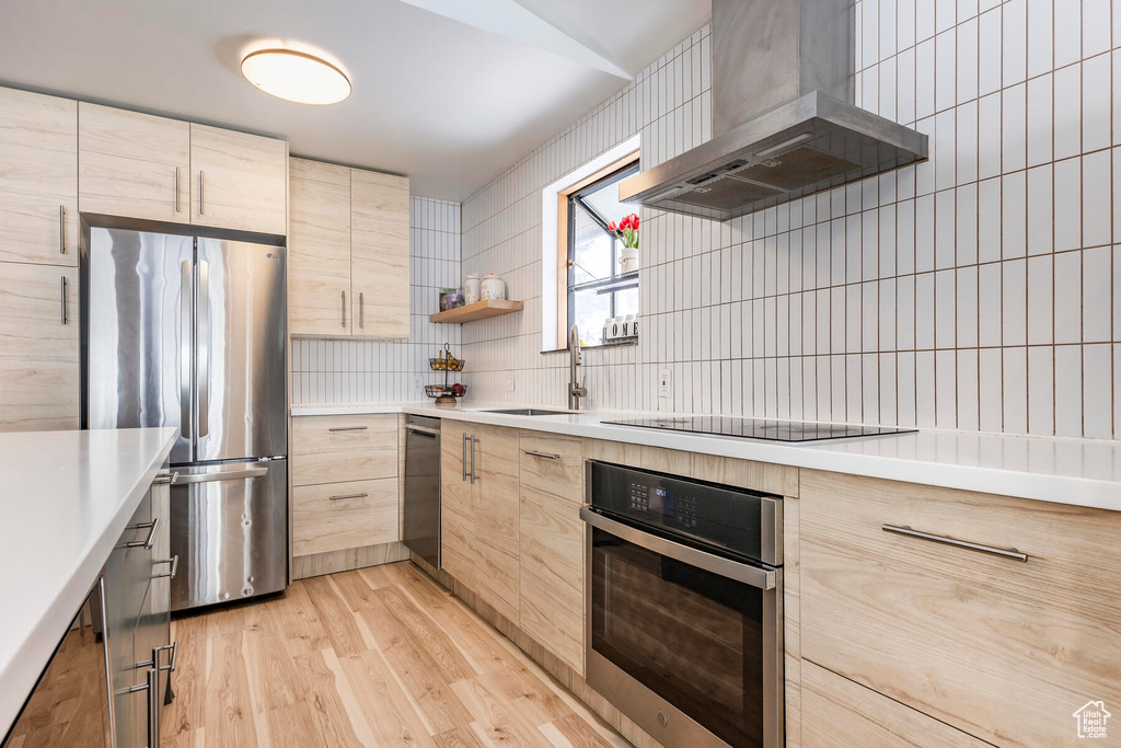 Kitchen featuring light hardwood / wood-style floors, appliances with stainless steel finishes, wall chimney exhaust hood, and light brown cabinets