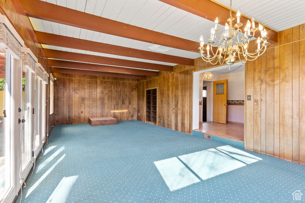 Carpeted empty room with a notable chandelier, beam ceiling, and wood walls