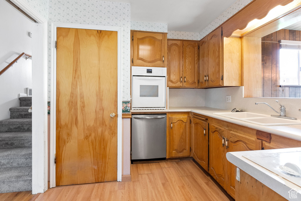 Kitchen featuring sink, white oven, dishwasher, and light hardwood / wood-style flooring