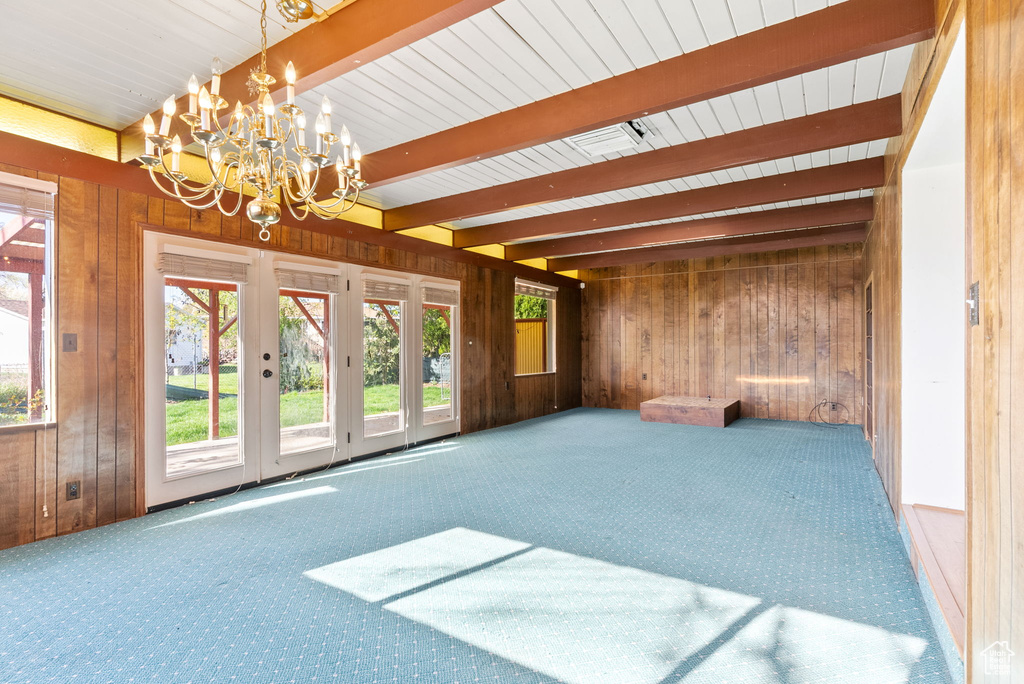 Carpeted spare room with french doors, wood walls, beam ceiling, and a notable chandelier