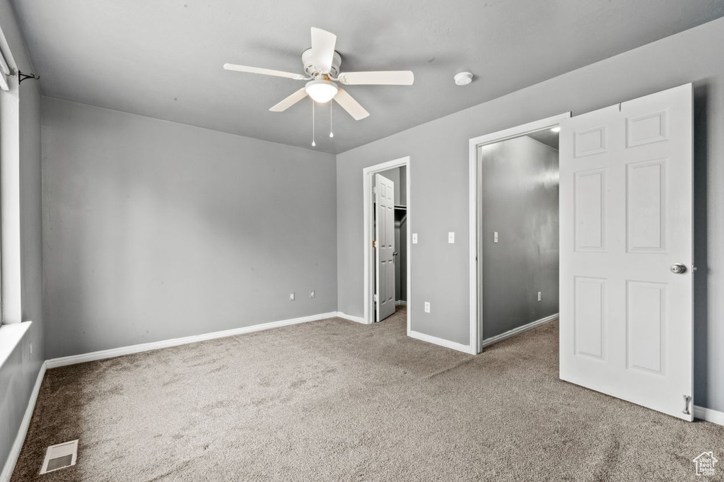 Unfurnished bedroom with a walk in closet, light colored carpet, and ceiling fan