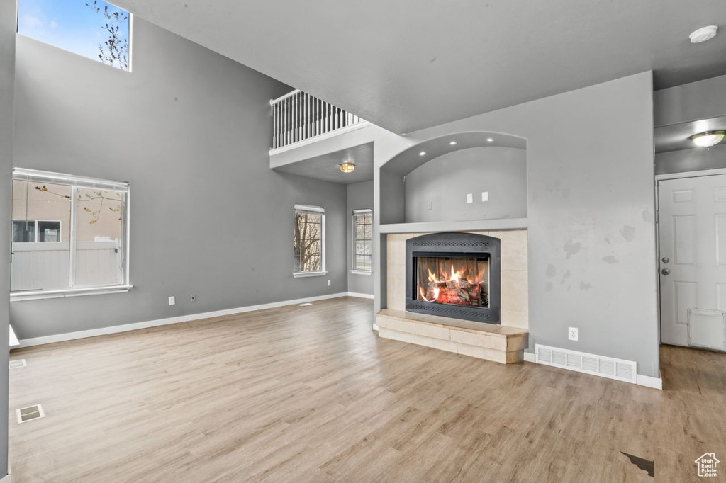 Unfurnished living room with a high ceiling, a tile fireplace, and light hardwood / wood-style flooring