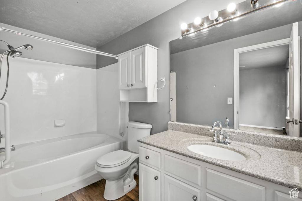Full bathroom featuring toilet, large vanity, hardwood / wood-style floors, and bathing tub / shower combination