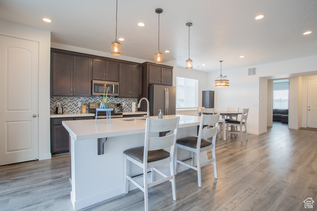 Kitchen featuring pendant lighting, a kitchen breakfast bar, appliances with stainless steel finishes, a center island with sink, and light hardwood / wood-style floors
