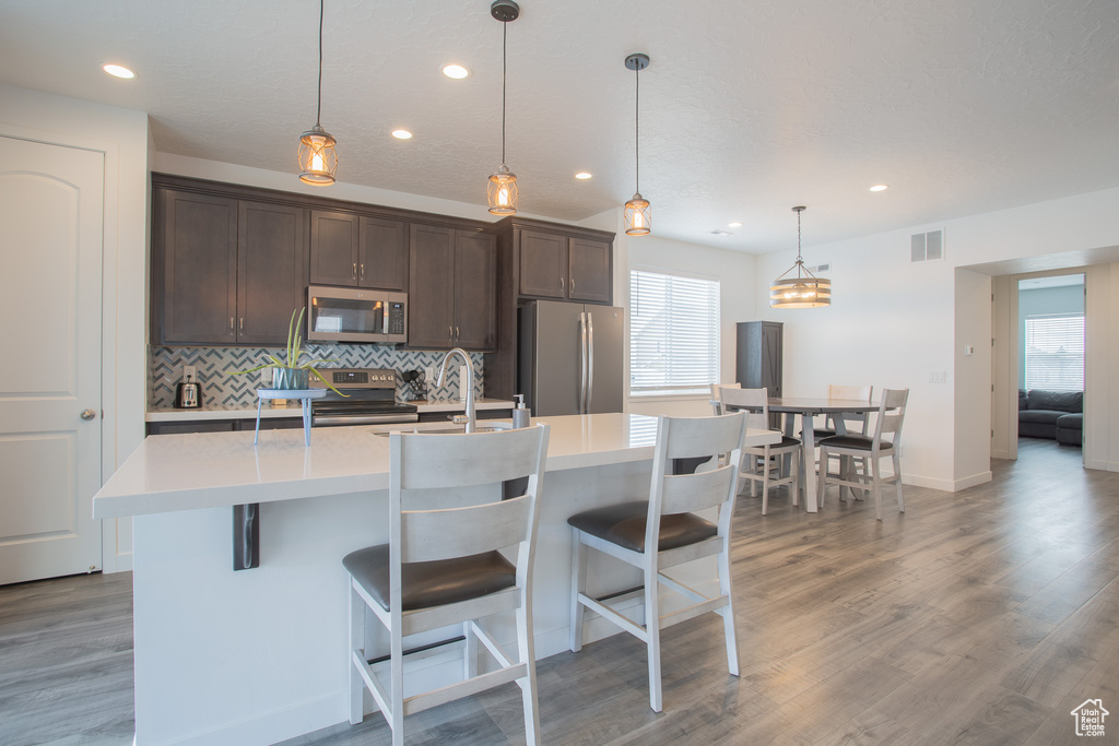 Kitchen with decorative light fixtures, hardwood / wood-style floors, a breakfast bar area, appliances with stainless steel finishes, and a kitchen island with sink