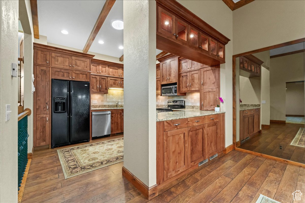 Kitchen featuring beam ceiling, stainless steel appliances, dark wood-type flooring, and light stone counters