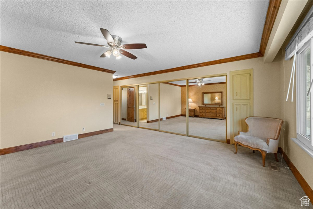 Interior space with ceiling fan, a textured ceiling, and crown molding