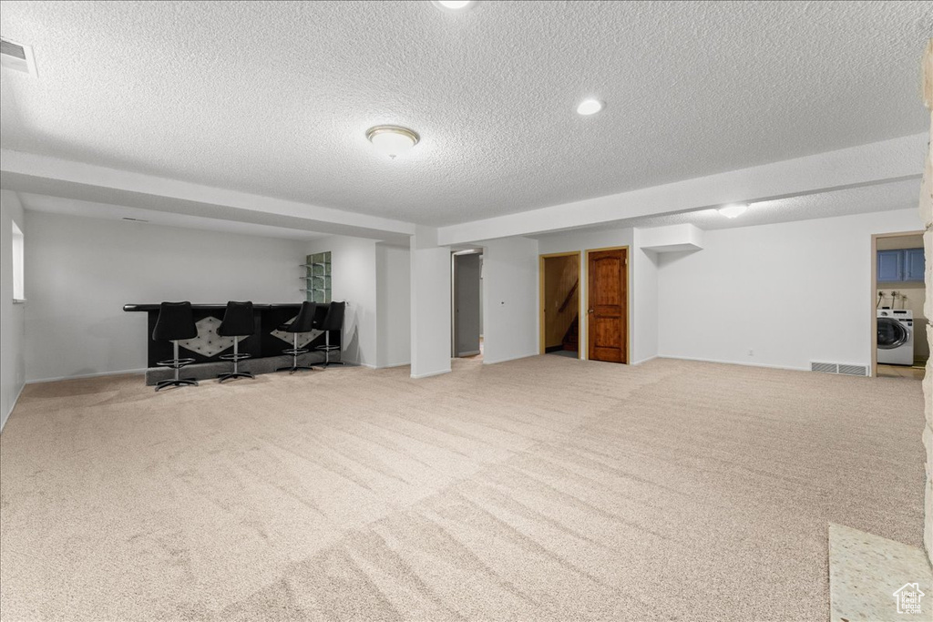 Living room featuring light carpet, a textured ceiling, and washer / dryer