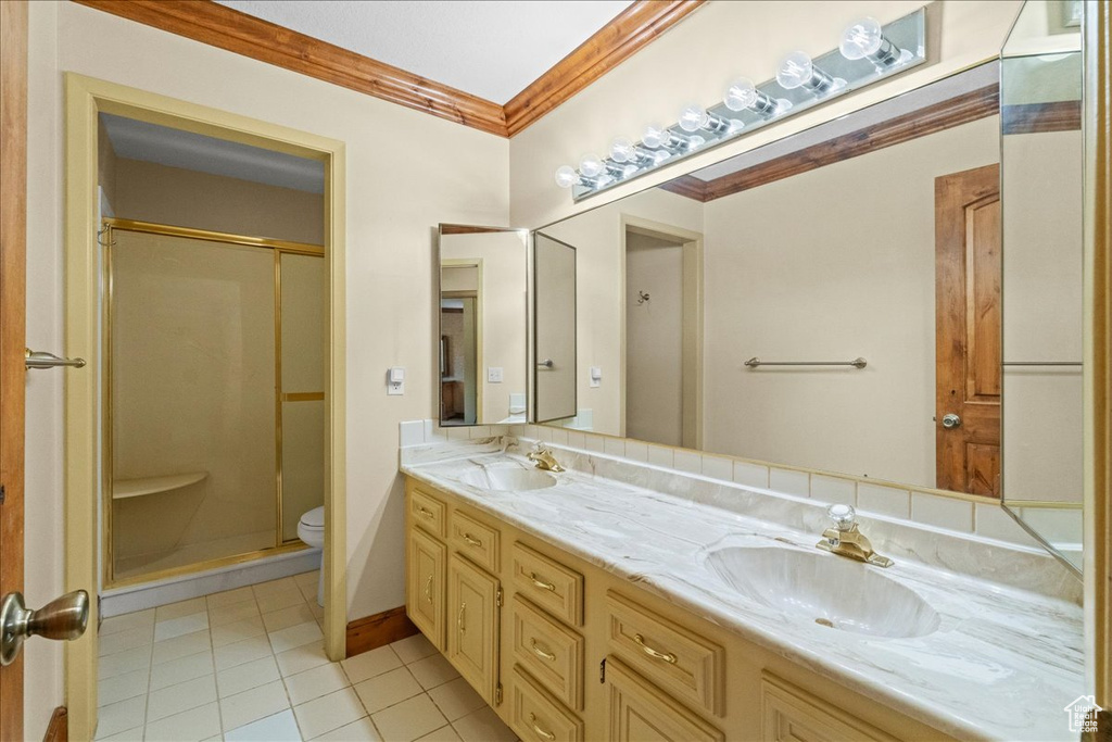 Bathroom featuring toilet, double sink vanity, crown molding, a shower with door, and tile flooring
