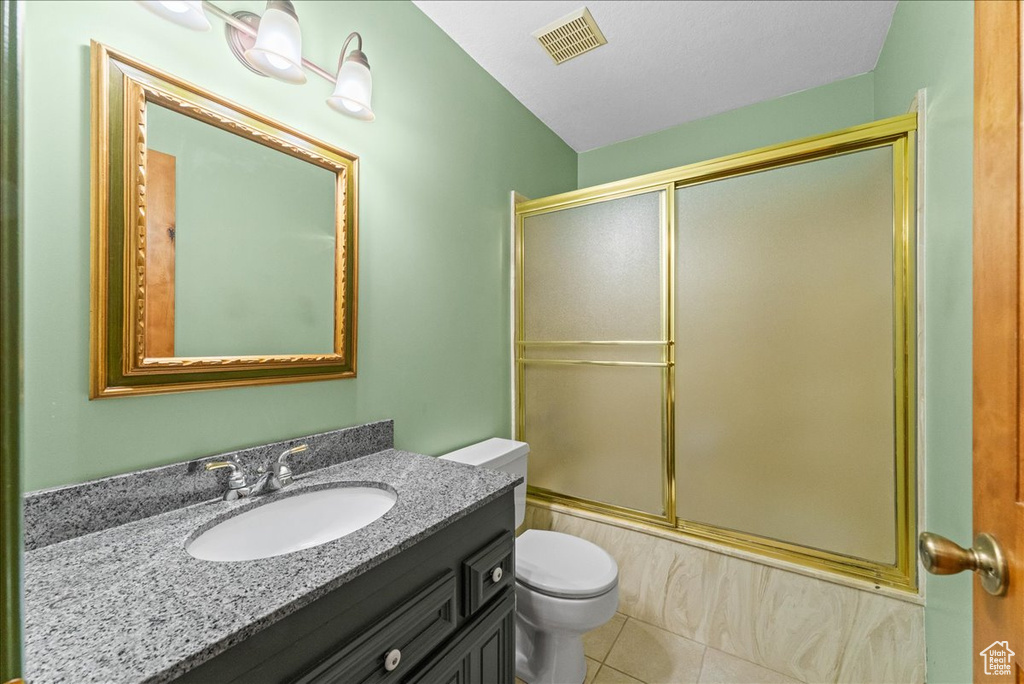 Full bathroom featuring bath / shower combo with glass door, tile floors, large vanity, and toilet