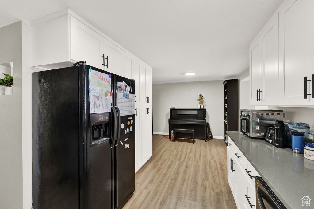 Kitchen featuring light hardwood / wood-style floors, black appliances, and white cabinetry