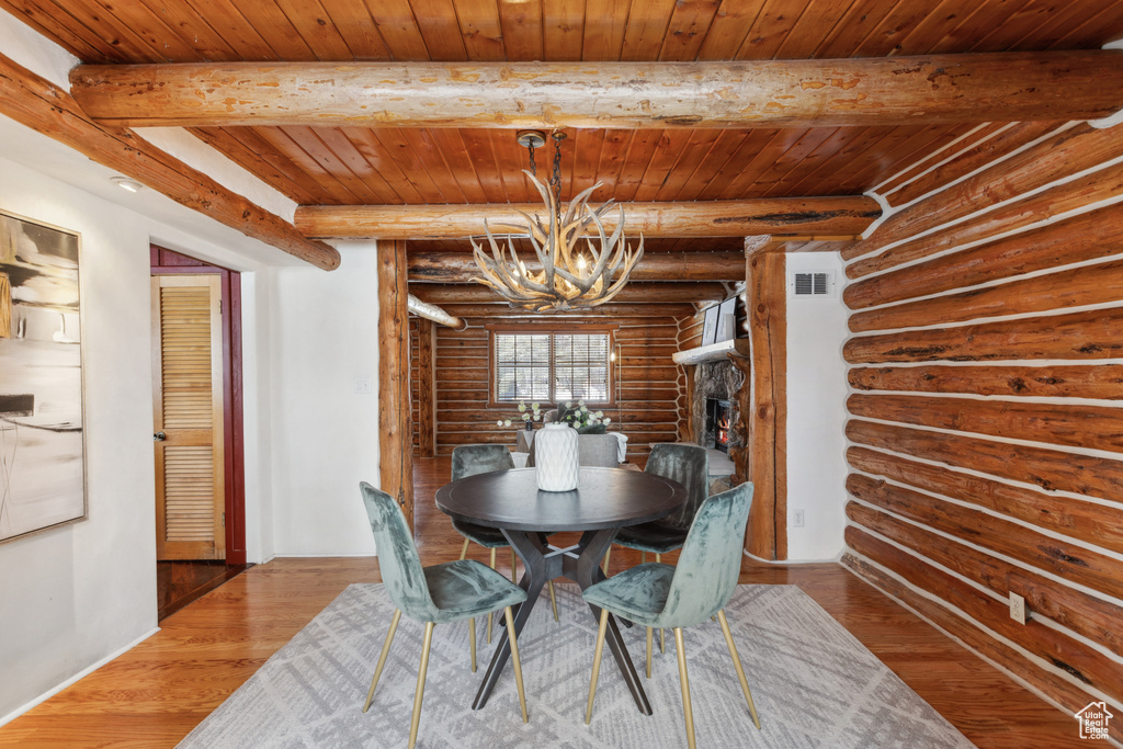 Unfurnished dining area featuring dark hardwood / wood-style floors, log walls, an inviting chandelier, wooden ceiling, and beam ceiling