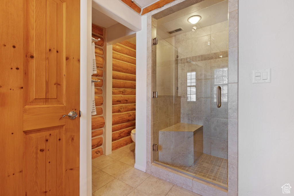 Bathroom with an enclosed shower, log walls, toilet, and tile flooring