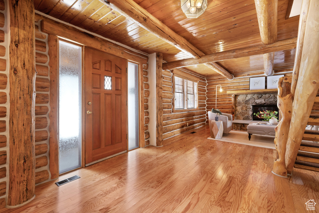 Entrance foyer with beamed ceiling, light hardwood / wood-style flooring, wooden ceiling, rustic walls, and a fireplace
