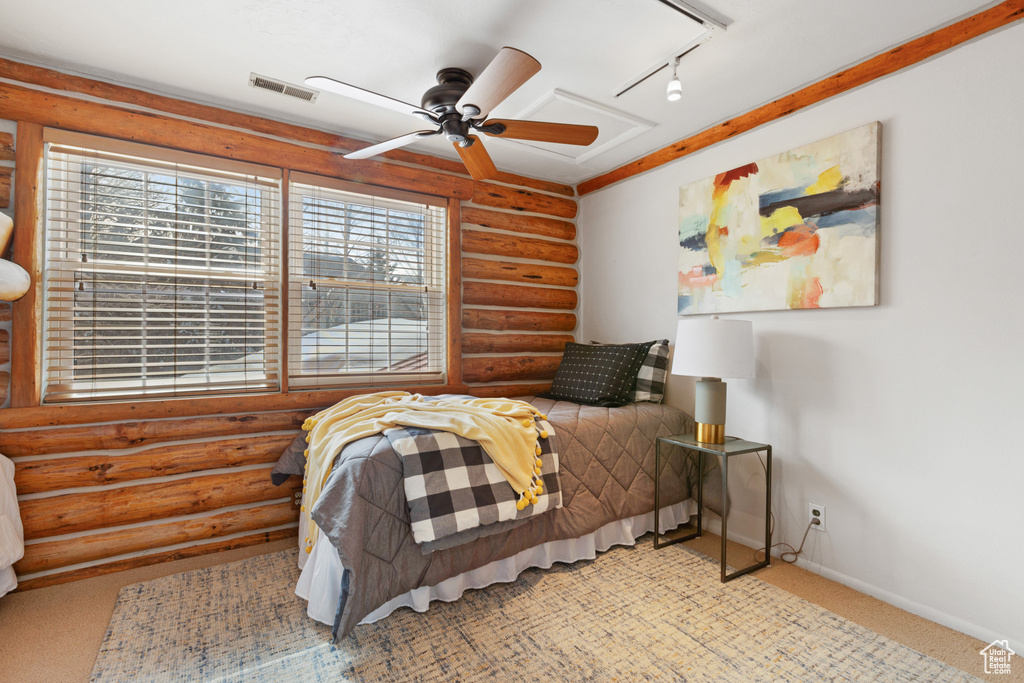 Carpeted bedroom featuring rustic walls, ceiling fan, and track lighting