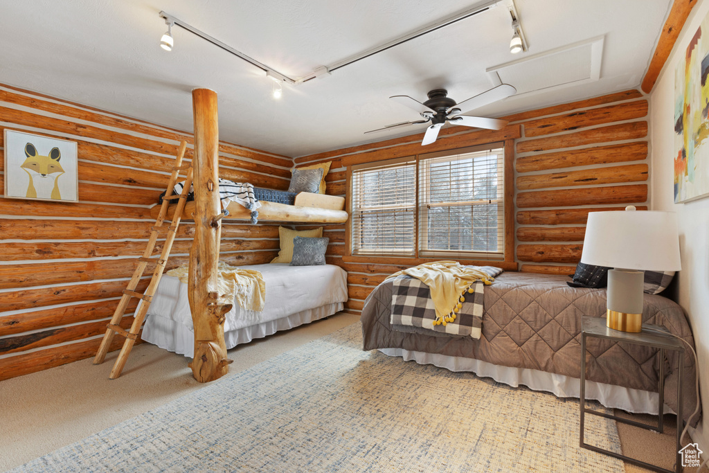 Carpeted bedroom with rustic walls, ceiling fan, and track lighting