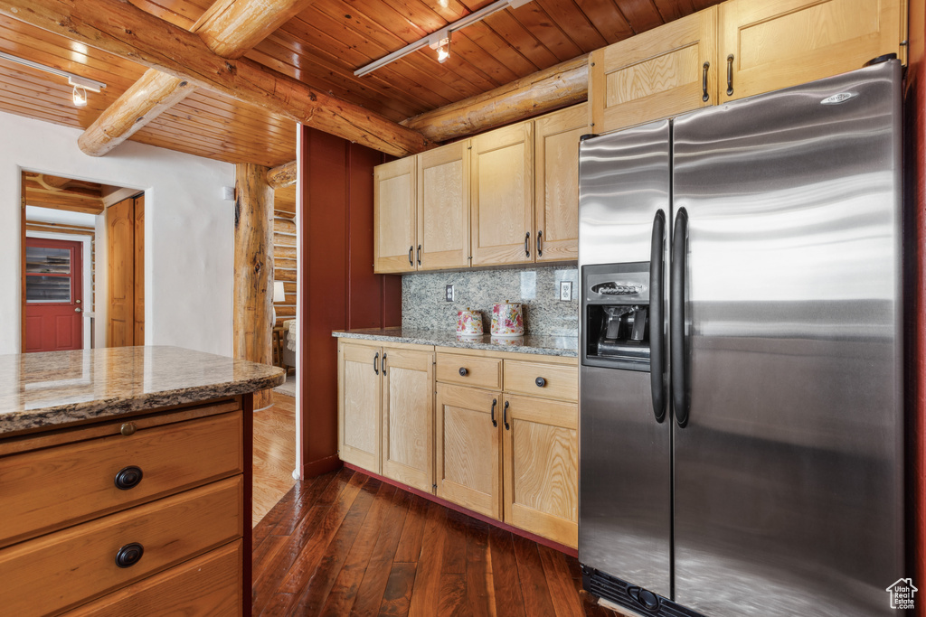 Kitchen with dark hardwood / wood-style floors, stainless steel fridge, light stone counters, rail lighting, and tasteful backsplash