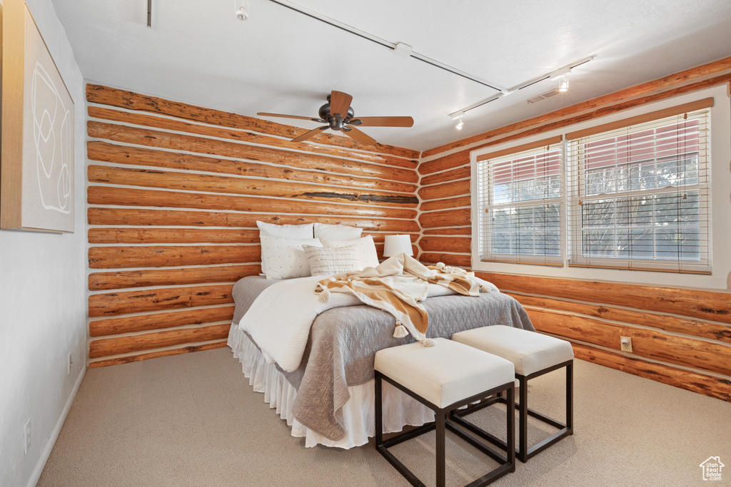 Bedroom with log walls, ceiling fan, rail lighting, and light colored carpet