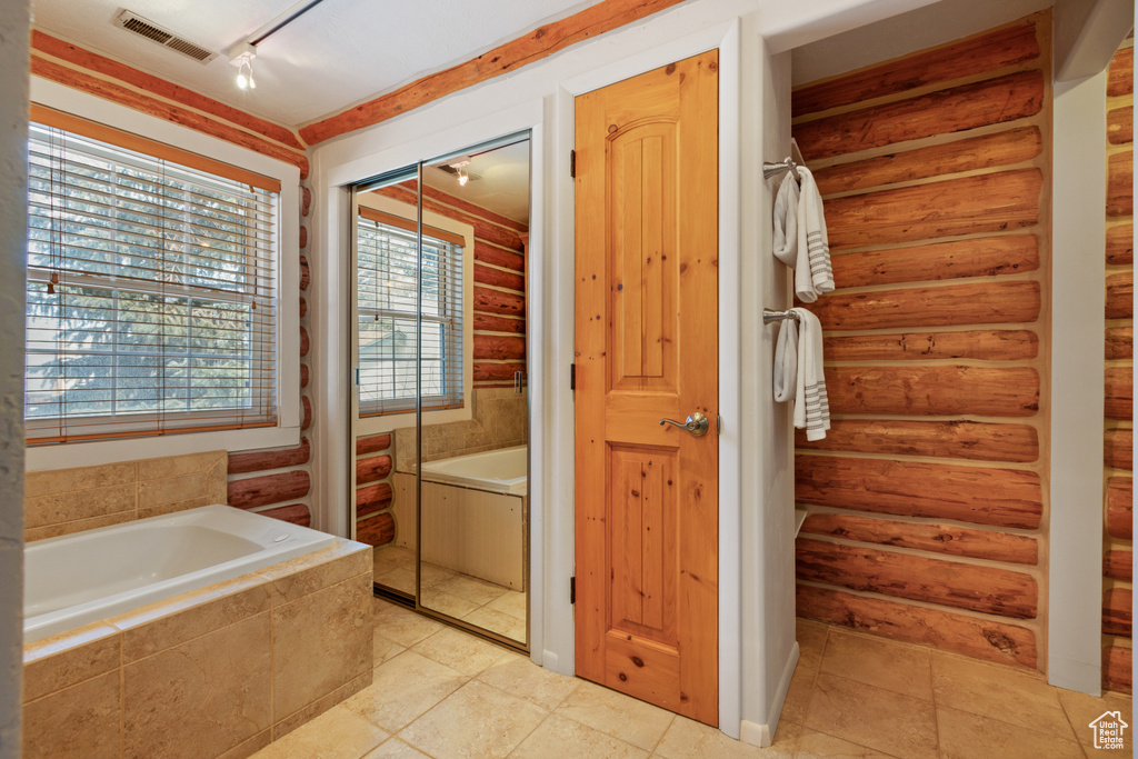 Bathroom with track lighting, tile floors, log walls, and tiled tub