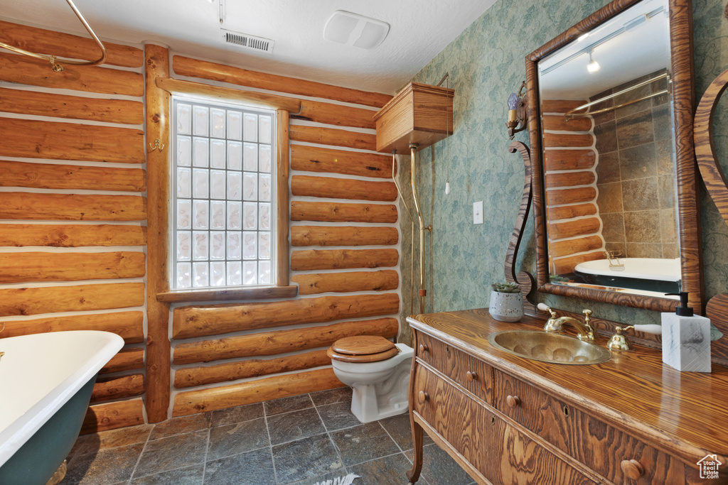 Bathroom with tile flooring, rustic walls, toilet, and vanity