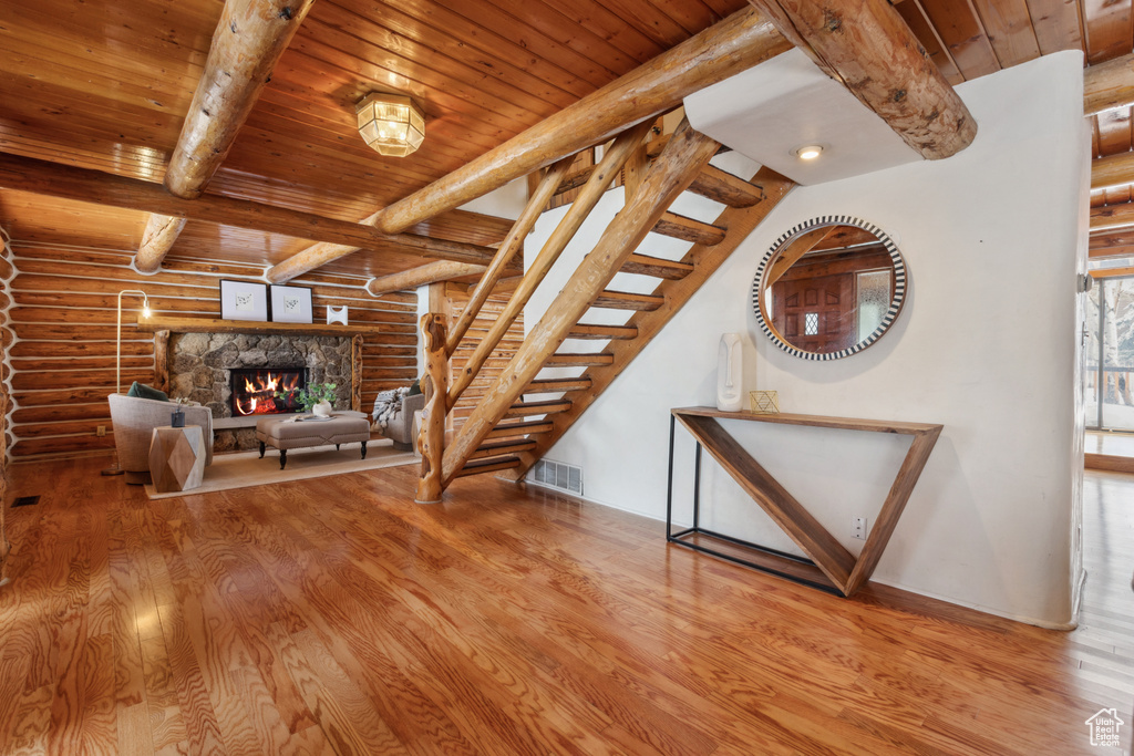Stairs featuring rustic walls, a stone fireplace, light wood-type flooring, and beamed ceiling