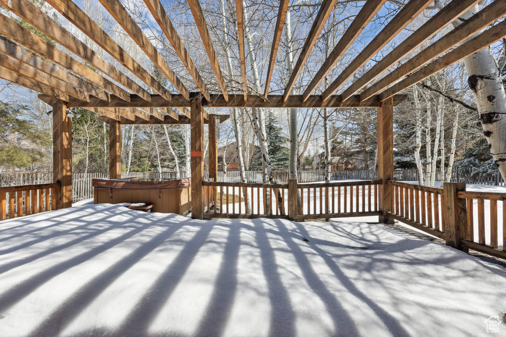 Snow covered deck featuring a hot tub and a pergola