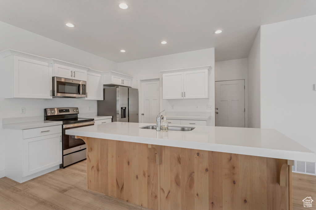 Kitchen featuring a center island with sink, appliances with stainless steel finishes, white cabinets, and light wood-type flooring