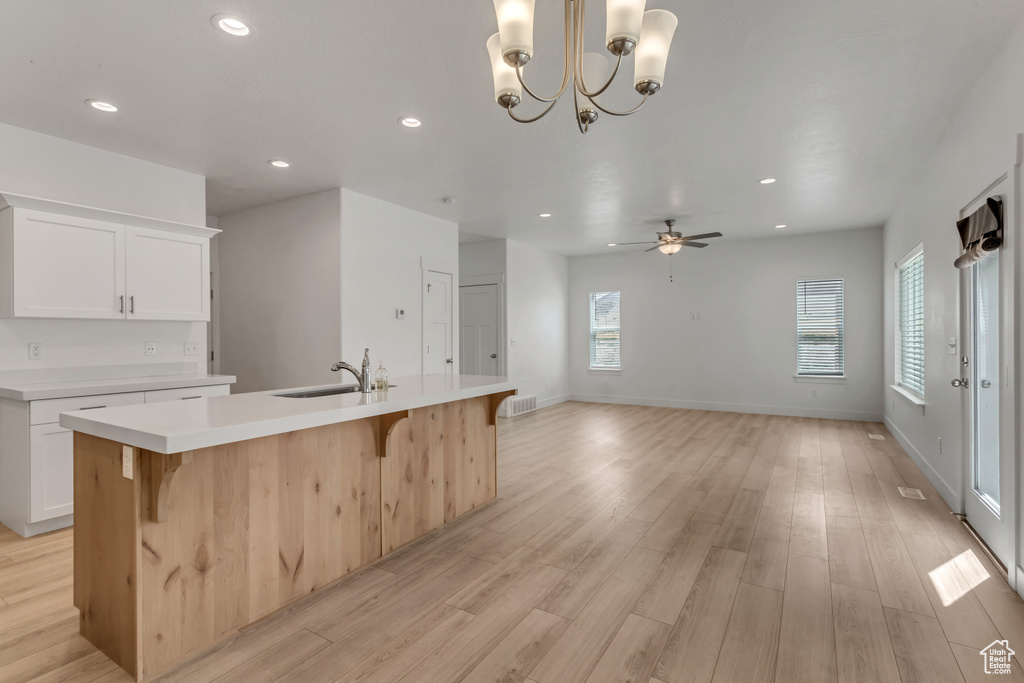Kitchen with a center island with sink, light hardwood / wood-style floors, ceiling fan with notable chandelier, and a healthy amount of sunlight