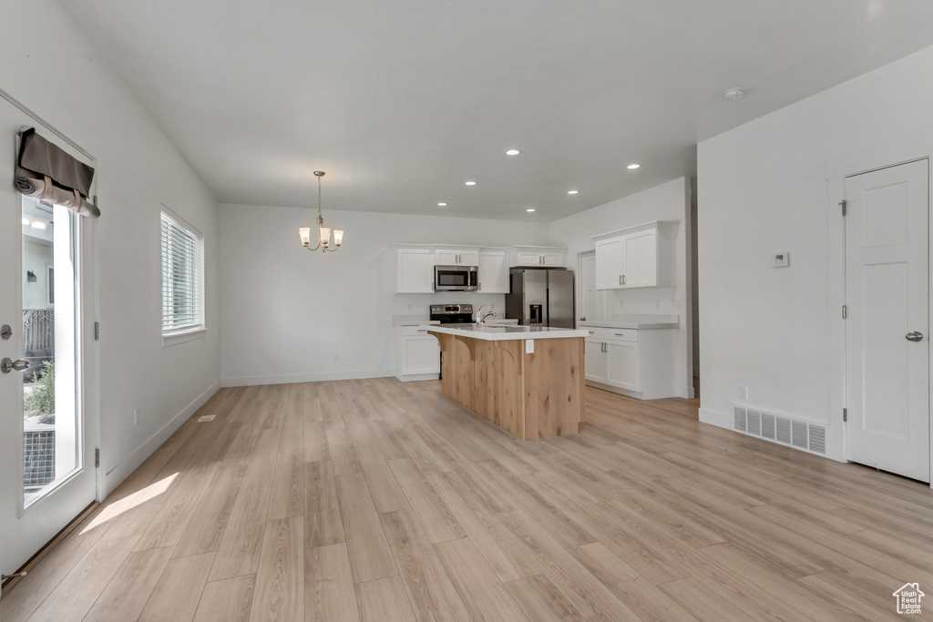 Kitchen featuring white cabinets, appliances with stainless steel finishes, decorative light fixtures, and light wood-type flooring