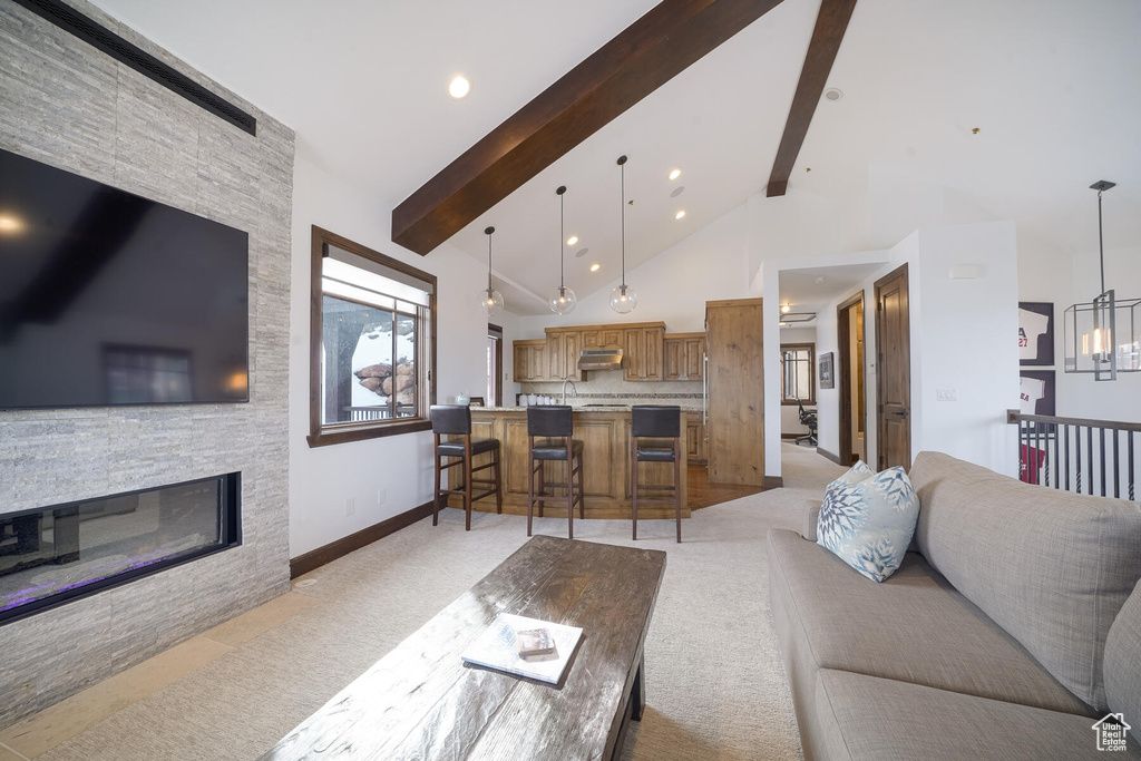Living room featuring an inviting chandelier, light carpet, beam ceiling, and a stone fireplace