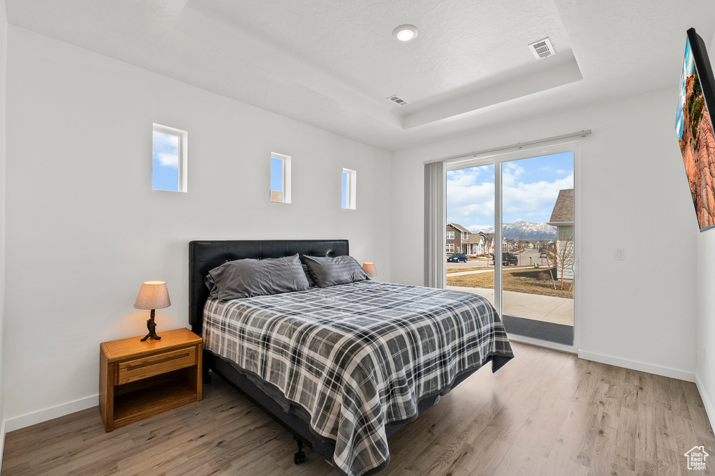 Bedroom featuring a tray ceiling, access to exterior, and light hardwood / wood-style flooring