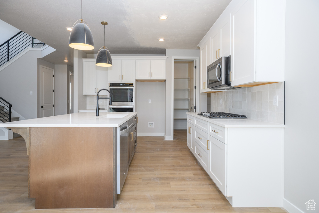 Kitchen featuring white cabinets, backsplash, light wood-type flooring, and pendant lighting