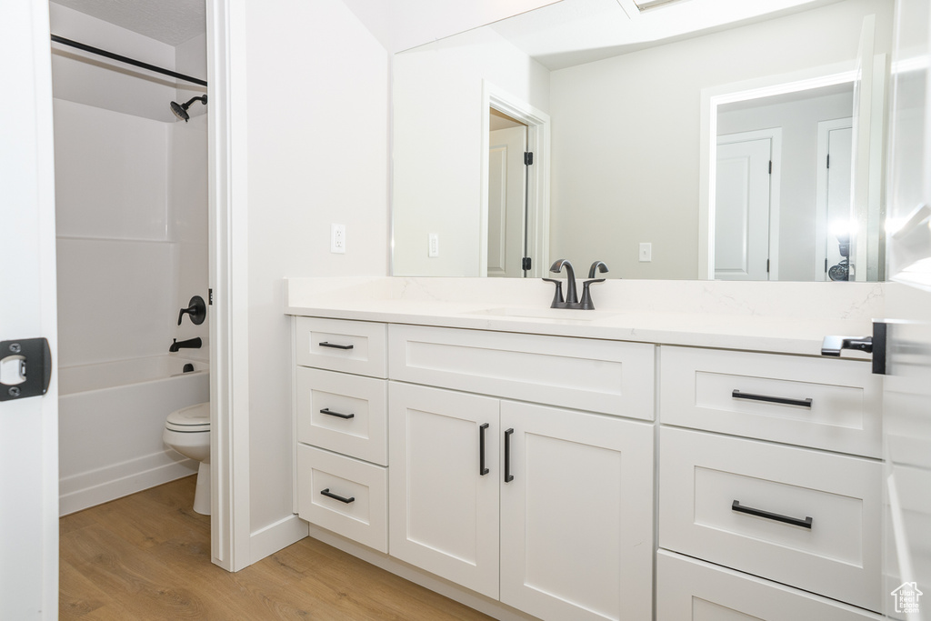 Full bathroom with shower / bathing tub combination, toilet, vanity with extensive cabinet space, and hardwood / wood-style floors