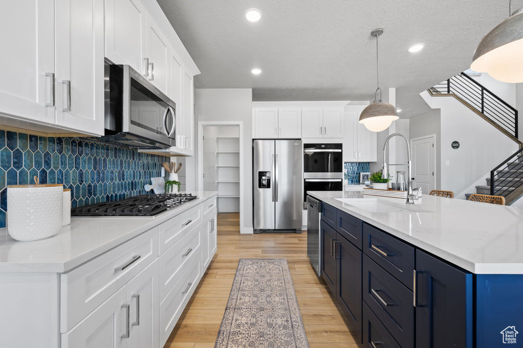 Kitchen featuring pendant lighting, white cabinets, backsplash, light hardwood / wood-style floors, and stainless steel appliances
