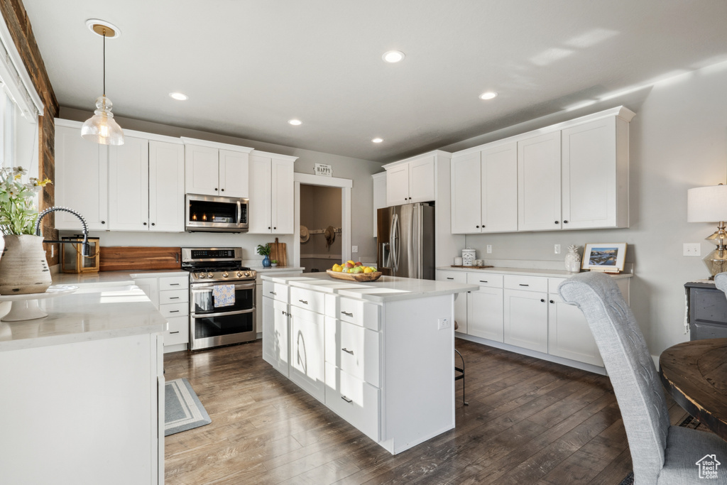 Kitchen with dark hardwood / wood-style floors, pendant lighting, stainless steel appliances, white cabinetry, and a center island