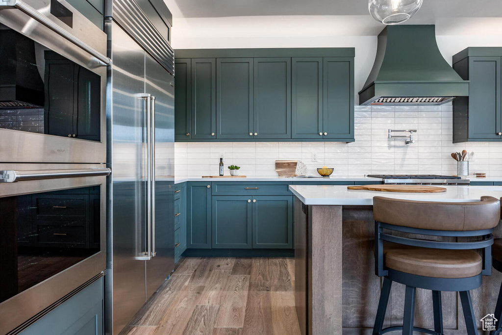 Kitchen with premium range hood, tasteful backsplash, dark wood-type flooring, and appliances with stainless steel finishes
