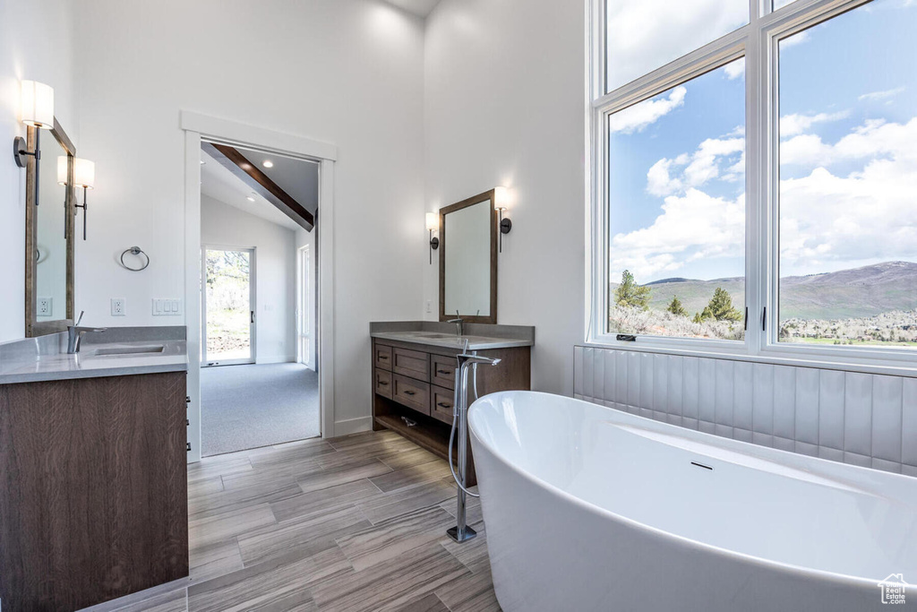 Bathroom with plenty of natural light, a washtub, vaulted ceiling, and dual bowl vanity