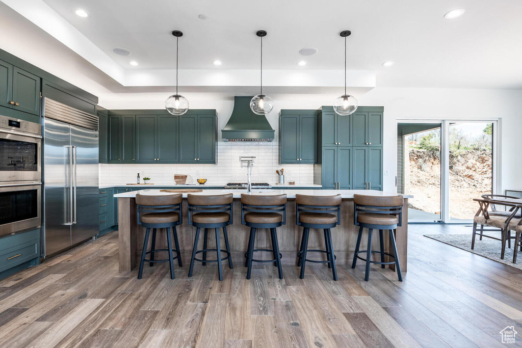 Kitchen with decorative light fixtures, appliances with stainless steel finishes, premium range hood, tasteful backsplash, and a breakfast bar area