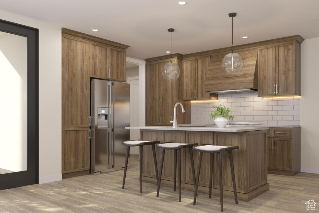 Kitchen with light hardwood / wood-style floors, a center island, decorative light fixtures, tasteful backsplash, and high end fridge