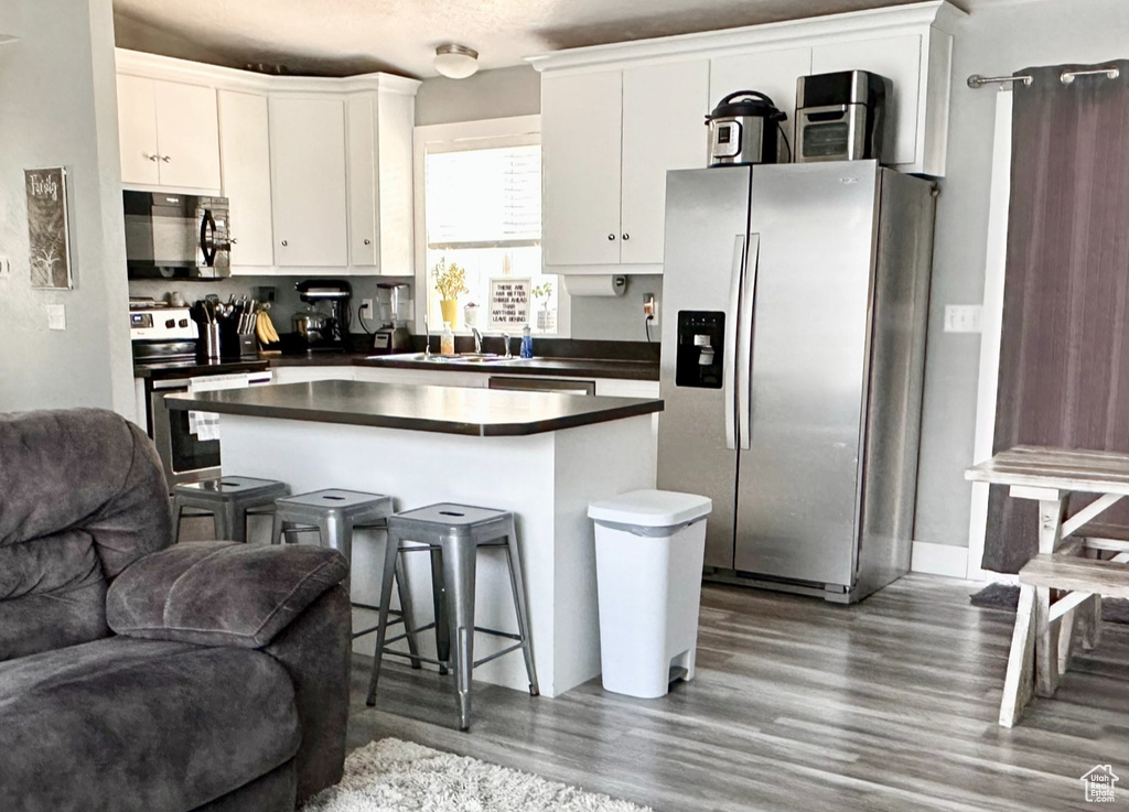 Kitchen featuring white cabinets, a center island, appliances with stainless steel finishes, and dark hardwood / wood-style flooring
