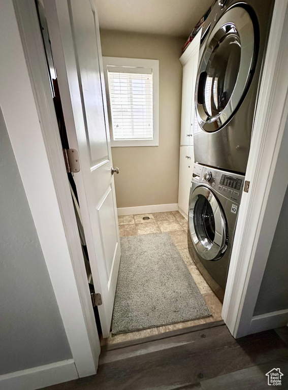 Clothes washing area with dark tile flooring and stacked washer and dryer