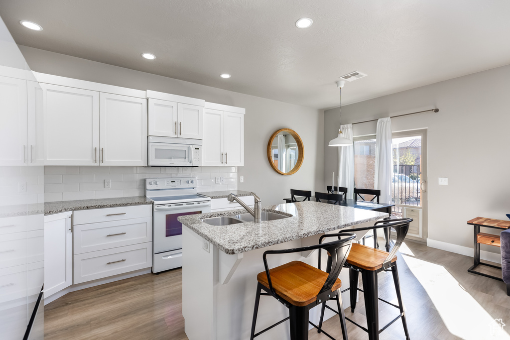 Kitchen with light hardwood / wood-style flooring, pendant lighting, white appliances, and sink